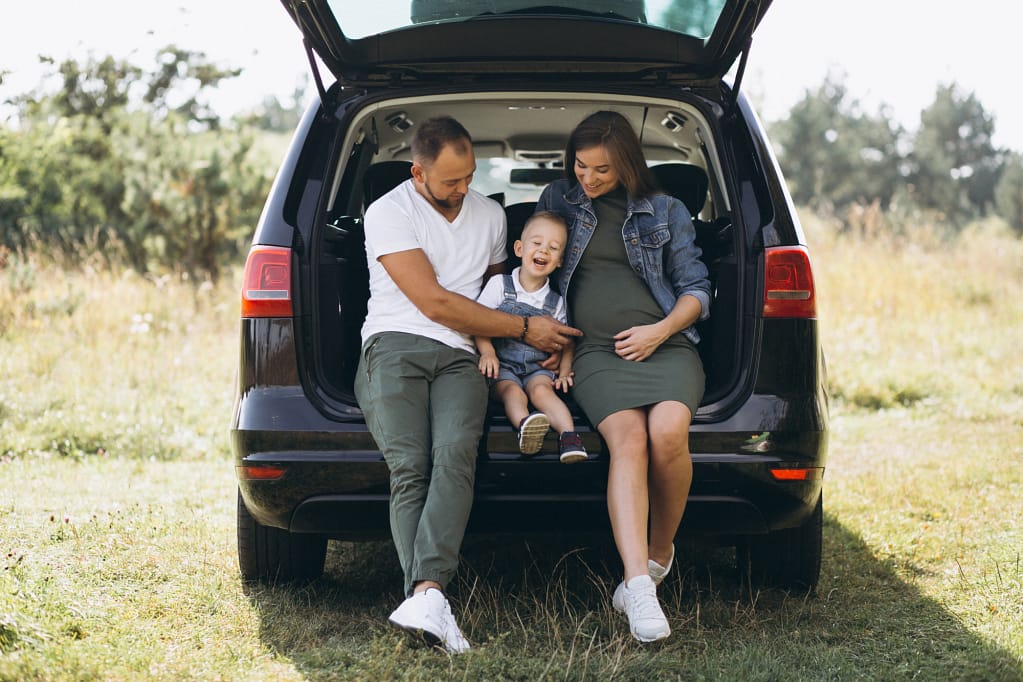 Family sitting in the open trunk of an SUV, enjoying time together outdoors—ideal vehicle choice for big families on a budget.