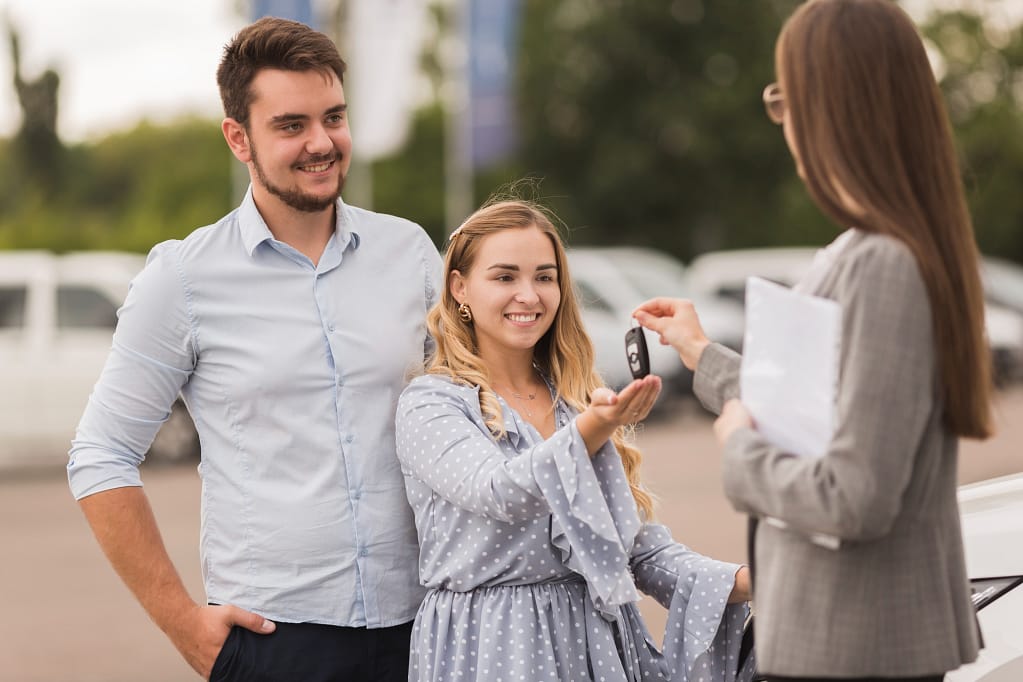 Happy couple selling their car for recycling, receiving keys and finalizing the process at a scrap yard.